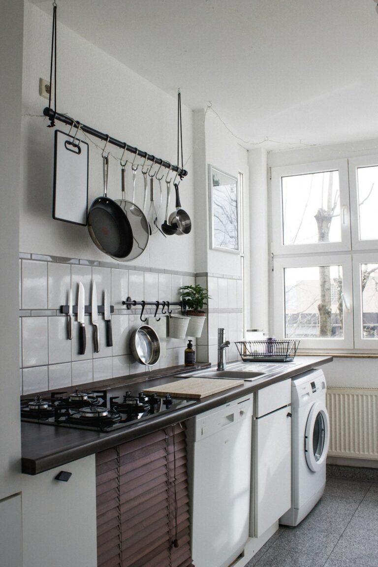 A person rinsing vegetable scraps into a kitchen sink with a garbage disposal switch nearby.
