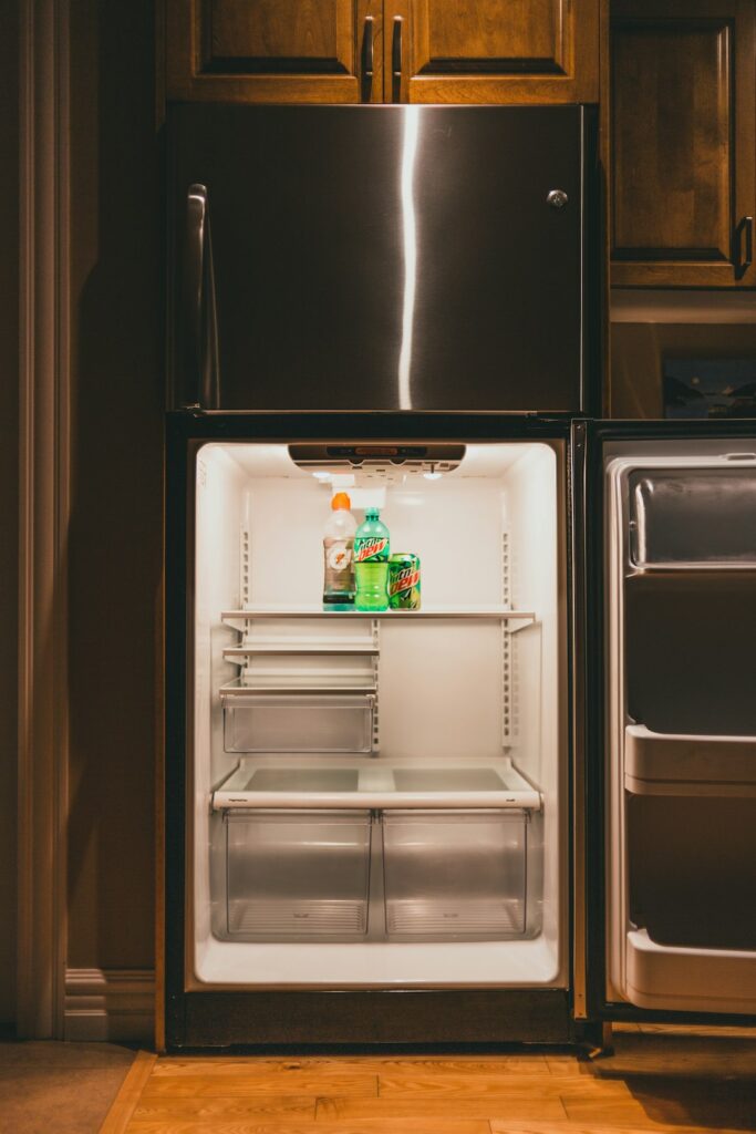 A person thoroughly cleaning removable fridge shelves at a kitchen sink.