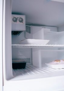 Person clearing thick frost buildup from a home freezer shelf with a plastic spatula