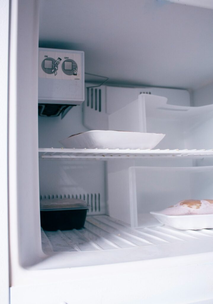 Person clearing thick frost buildup from a home freezer shelf with a plastic spatula