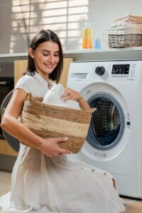 Person removing pet hair from a blanket beside an open washer and dryer.
